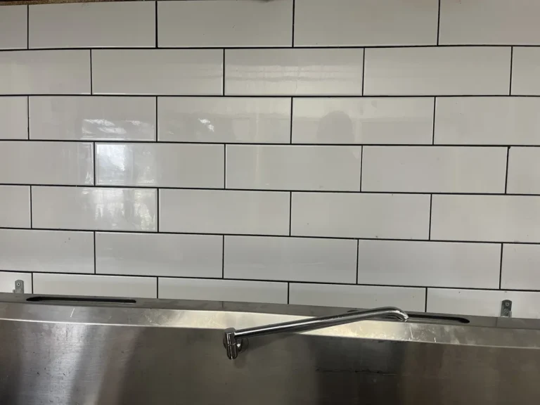 Stainless steel sink under white tiled wall.