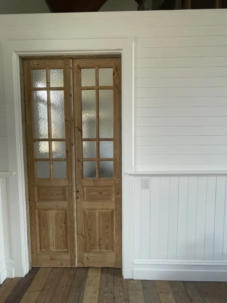 Wooden double doors with frosted glass in white room.